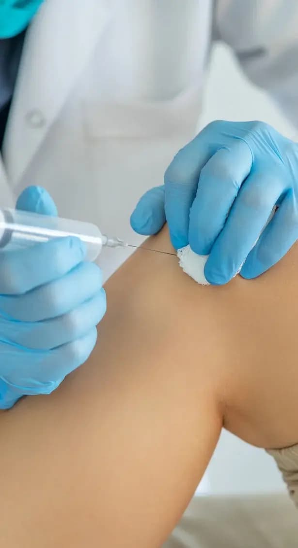 Gloved hands administering an injection into a patient’s knee